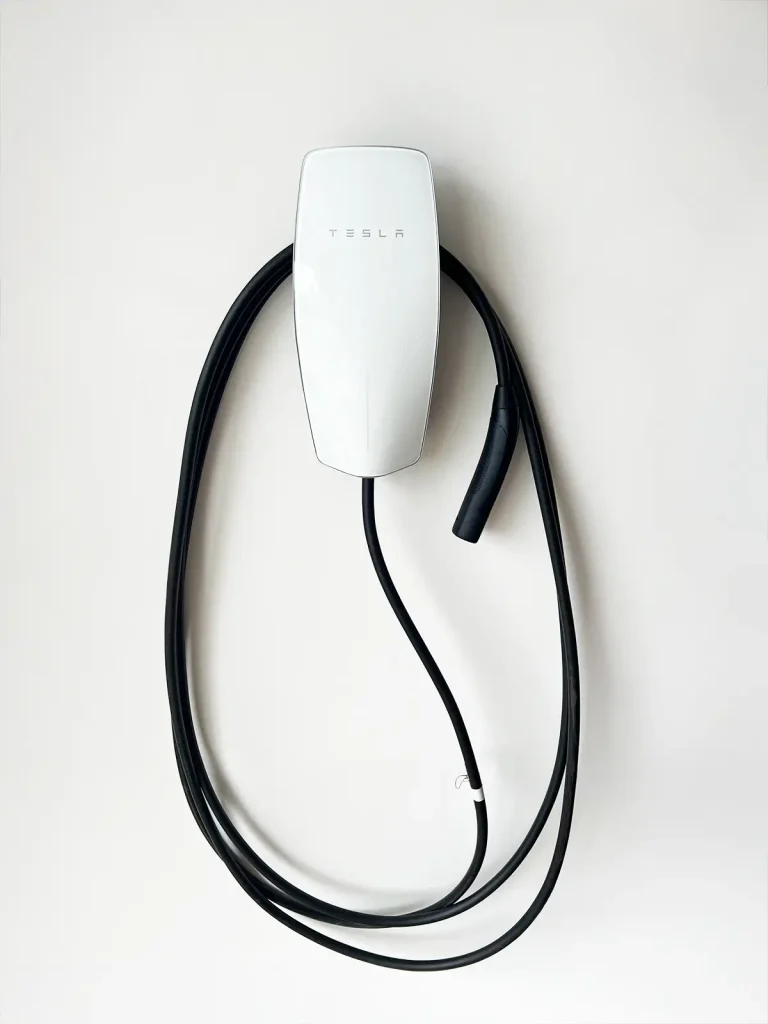 White Telsa at home charging station with a black cord